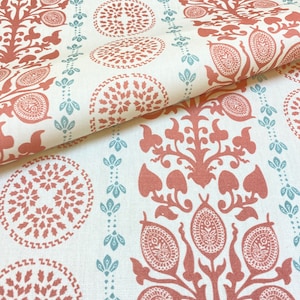 May include: Cream-colored fabric with a repeating pattern of rust-colored floral and circular designs. The design includes stylized trees, medallions, and vertical rows of small blue-green floral elements. The fabric is folded, showing the pattern's continuity.