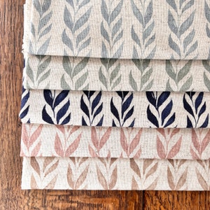 May include: Five fabric swatches featuring a repeating pattern of stylised leaves. The swatches are stacked on top of each other, with the top swatch being a light grey with blue-green leaves, followed by a light grey with green leaves, then a light grey with dark blue leaves, then a light grey with pink leaves, and finally a light grey with brown leaves.