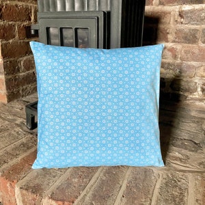 May include: A light blue throw pillow with a white floral pattern. The pillow is sitting on a brick surface.