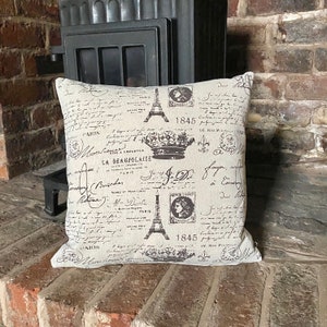 May include: A beige cushion with a black and white print of the Eiffel Tower, a crown, and handwritten text in French. The text includes the year "1845" and the words "La Beaujolaise" and "Paris".