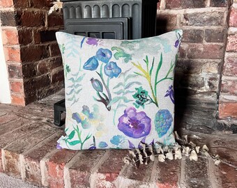 May include: A decorative cushion with a floral pattern featuring blue, purple, and green watercolour flowers on a white background.