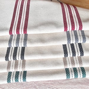 Puede incluir: Conjunto de cinco toallas de cocina con rayas de diferentes colores. Las toallas están hechas de tela de lino natural y tienen un aspecto rústico. Las rayas son rojas, grises, negras, beige y verdes.