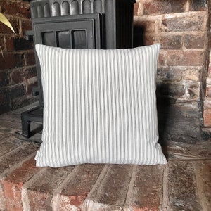 May include: A white pillow with thin black stripes. The pillow is sitting on a brick surface.