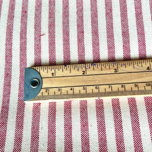 Może przedstawiać: Tkanina w czerwono-białe paski z drewnianym linijką o długości 25,4 cm. Tkanina ma drobną, r&oacute;wnomierną strukturę.