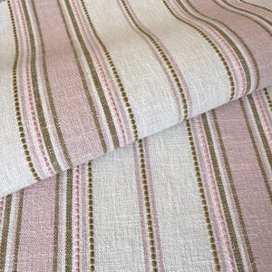 May include: A woven fabric featuring a repeating vertical striped pattern in shades of soft pink, off-white, and muted olive green. The textile displays a visible textured weave with thin, raised stitch-like lines running parallel throughout the design.
