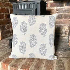 May include: A cream coloured throw pillow with a blue floral pattern. The pillow is made of linen and has a square shape.