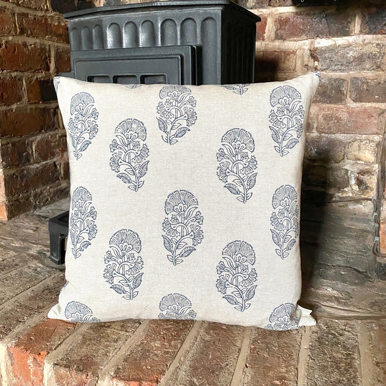 May include: A cream coloured throw pillow with a blue floral pattern. The pillow is made of linen and has a square shape.