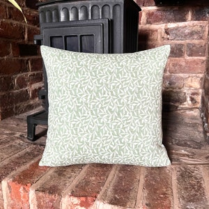 May include: A green cushion with a white leaf pattern. The cushion is sitting on a brick surface.