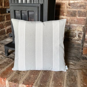 May include: A gray and white striped throw pillow with a subtle texture. The pillow is sitting in front of a brick fireplace.