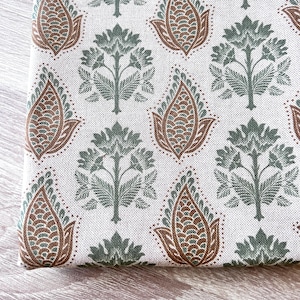 Puede incluir: Primer plano de una tela doblada con un patrón repetitivo. El diseño presenta motivos florales y paisley estilizados en tonos marrón y verde sobre un fondo crema. La tela tiene una apariencia texturizada.