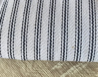 May include: Close-up of a white fabric with thin black stripes. The fabric is folded over, showing the texture of the weave.