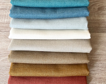 May include: A stack of eight fabric swatches in various colors, including teal, blue, gray, beige, brown, gold, and red. The swatches are arranged from darkest to lightest.