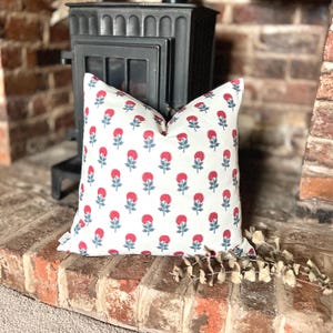 Puede incluir: Una almohada blanca con un patrón floral rojo y azul. La almohada está sentada sobre una superficie de ladrillo frente a una chimenea.