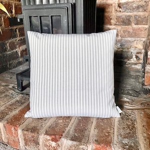 May include: A white pillow with thin black stripes. The pillow is sitting on a brick surface.