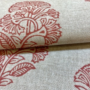 May include: Close-up of a fabric with a repeating pattern of red floral designs on a beige background.