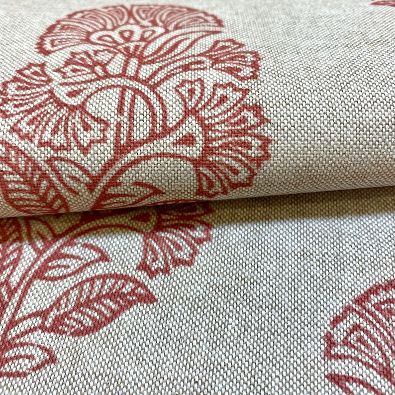May include: Close-up of a fabric with a repeating pattern of red floral designs on a beige background.