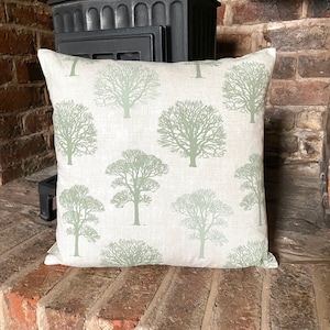 May include: A light green and white cushion with a repeating pattern of stylised trees. The cushion is made of a soft, textured fabric.