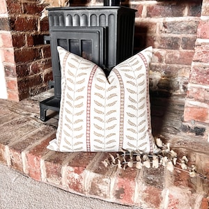 May include: A white cushion with a brown and red floral pattern. The cushion is sitting on a brick fireplace hearth.