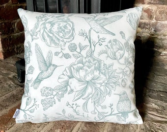 Puede incluir: Una almohada blanca con un patrón floral azul claro que presenta colibríes y rosas. La almohada tiene una estética vintage sutil.