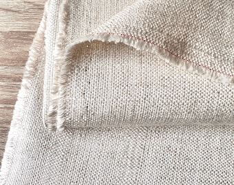 May include: A close-up of a piece of natural linen fabric with a raw edge. The fabric is folded over itself, showing the texture and weave of the material.