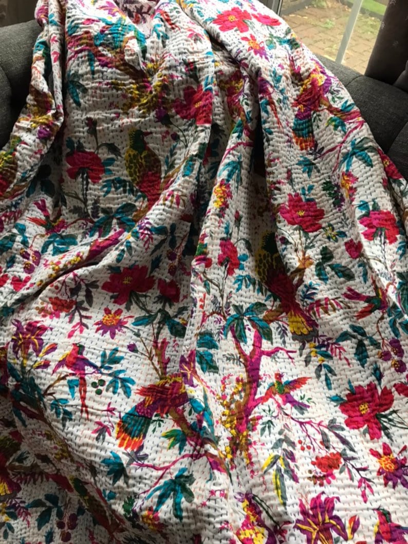 May include: White cotton quilt with a floral and bird print. The quilt features a variety of colors, including pink, red, blue, green, and yellow. The birds are depicted in a variety of poses, including flying, perched, and singing.
