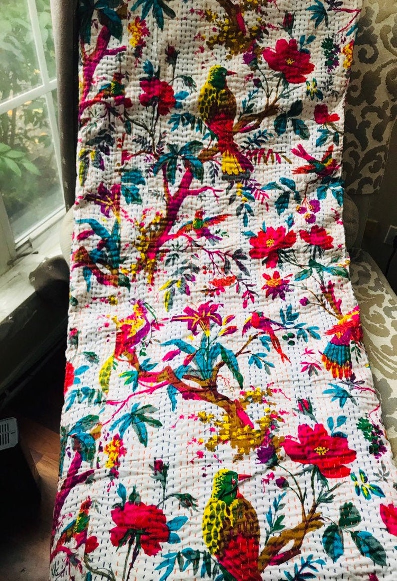 May include: A white kantha quilt with a floral and bird pattern. The quilt features pink, yellow, green, and blue colors. The quilt is made of cotton and is hand-stitched.