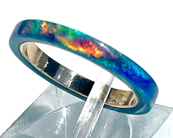 May include: A thin gold band ring with a blue, green, and iridescent opal inlay.