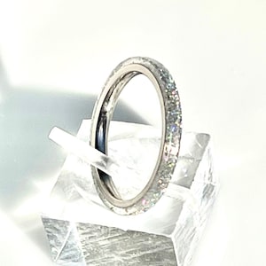 Op de afbeelding: Een zilveren ring met een glinsterende band op een heldere acryl ringhouder.