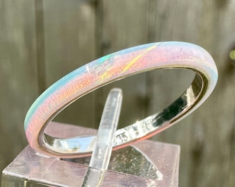 May include: A thin, iridescent ring with a pink, blue, and green color scheme. The ring is on a clear display stand.