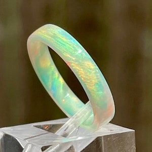 May include: A white opal ring with a green and yellow iridescent sheen. The ring is on a clear display stand.