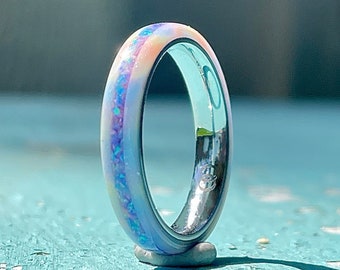 May include: A silver ring with a thin band of iridescent opal inlay. The opal is a mix of pink, blue, and white.