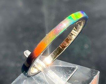 May include: A thin silver band ring with a colorful opal inlay. The opal displays a rainbow of colors, including red, orange, yellow, green, blue, and purple.