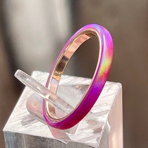 Op de afbeelding: Een dunne, regenboogkleurige roze ring met een gouden band. De ring staat op een transparante displaystandaard.