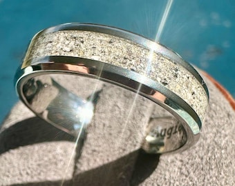 May include: A silver ring with a band of embedded sand. The ring is on a gray surface.