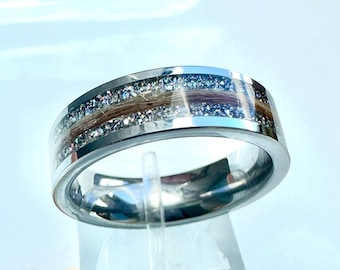 May include: A silver ring with a band of embedded hair and glitter. The ring is on a clear display stand.