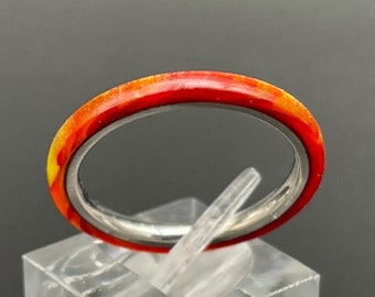 Op de afbeelding: Een dunne zilveren bandring met een rode en gele emaille coating. De ring wordt getoond op een heldere acryl ringstandaard.