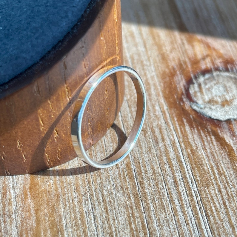 Op de afbeelding: Een dunne zilveren bandring op een houten oppervlak.