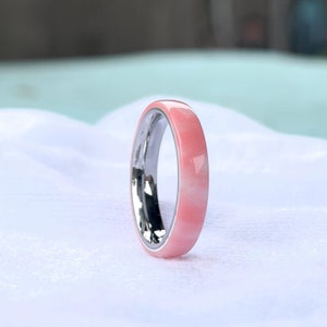 K&ouml;nnte beinhalten: Nahaufnahme eines Rings mit einem rosa Band und einem silbernen Innenraum. Der Ring ist vor einem wei&szlig;en Hintergrund platziert. Das rosa Band hat ein marmoriertes Aussehen.