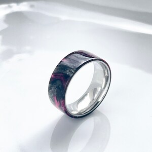 May include: A black and pink resin ring with a silver band. The resin has a marbled pattern.