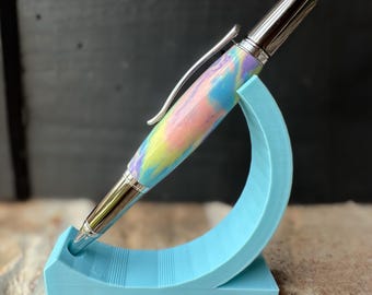 May include: A colorful, swirl-patterned pen with a silver clip and cap, displayed on a light blue pen stand.