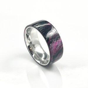 May include: A silver band ring with a black and pink marbled inlay. The inlay has a sparkly finish.