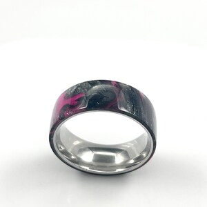 May include: A black and pink resin ring with a silver band. The resin has a swirling pattern.
