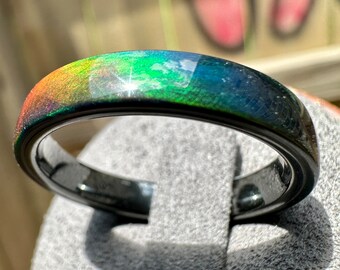 May include: A black ring with a rainbow iridescent finish. The ring is made of tungsten carbide and has a polished finish.