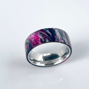 May include: A silver band ring with a black and pink marbled design.
