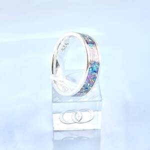May include: A silver band ring with a blue, purple, and pink iridescent inlay. The ring is marked with "925" on the inside of the band.