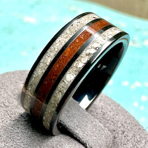 May include: A black tungsten carbide ring with two brown wood inlay bands and white fossilized bone inlay. The ring is polished and has a smooth finish.