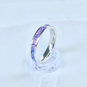 May include: A silver band ring with a thin band of purple and pink opal inlay.