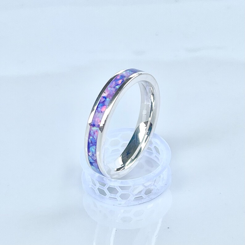 May include: A silver band ring with a thin band of purple and pink opal inlay.