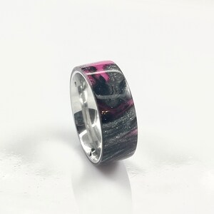 May include: A silver ring with a black and pink resin inlay. The resin has a swirling pattern and a glossy finish.