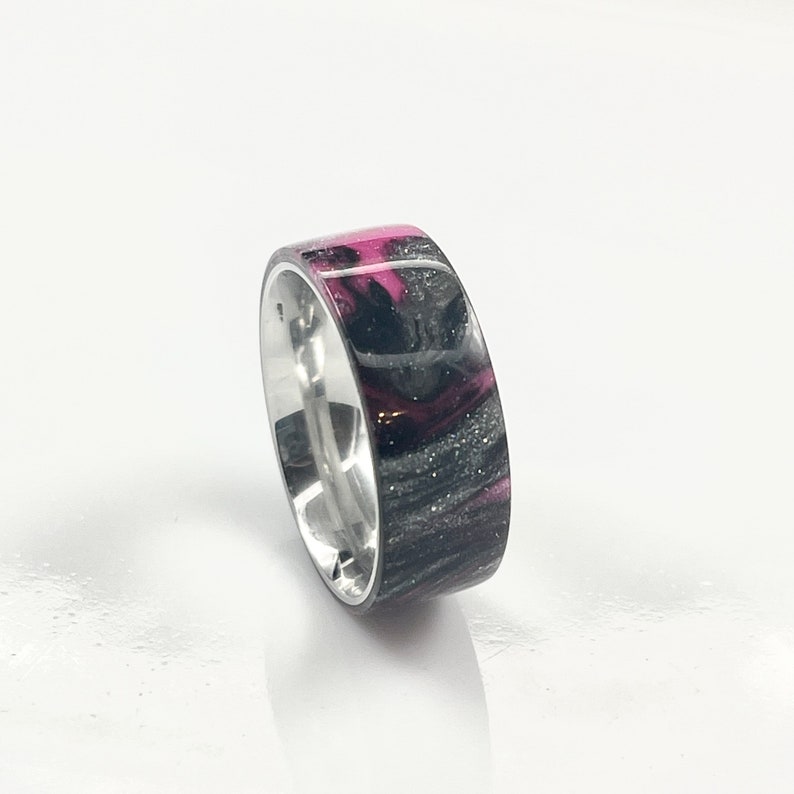 May include: A silver ring with a black and pink resin inlay. The resin has a swirling pattern and a glossy finish.